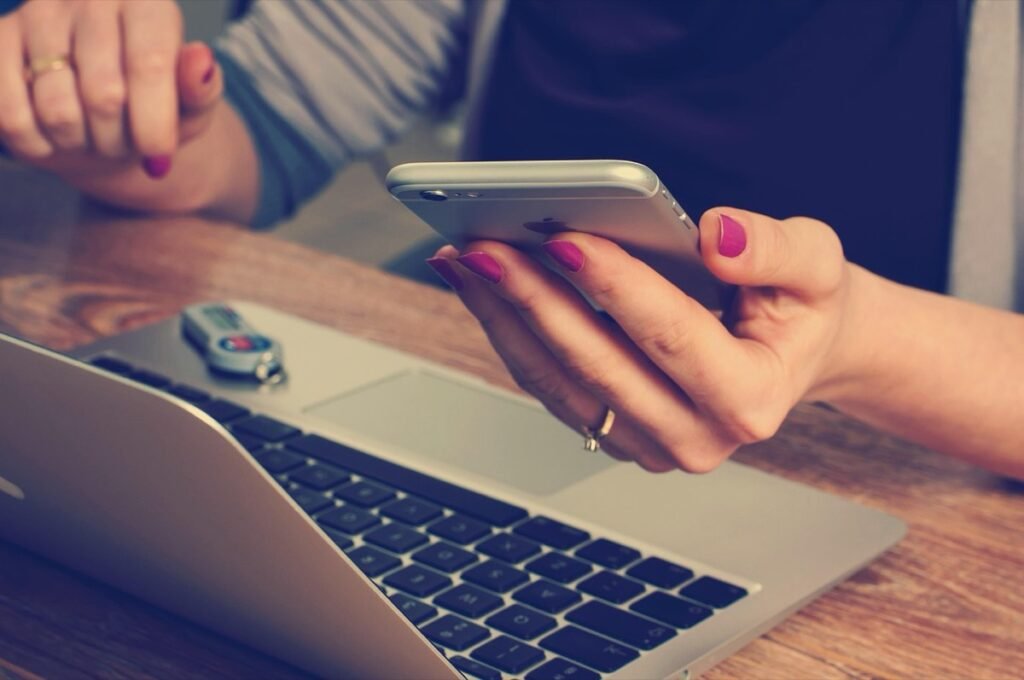 Person using a smartphone beside a laptop